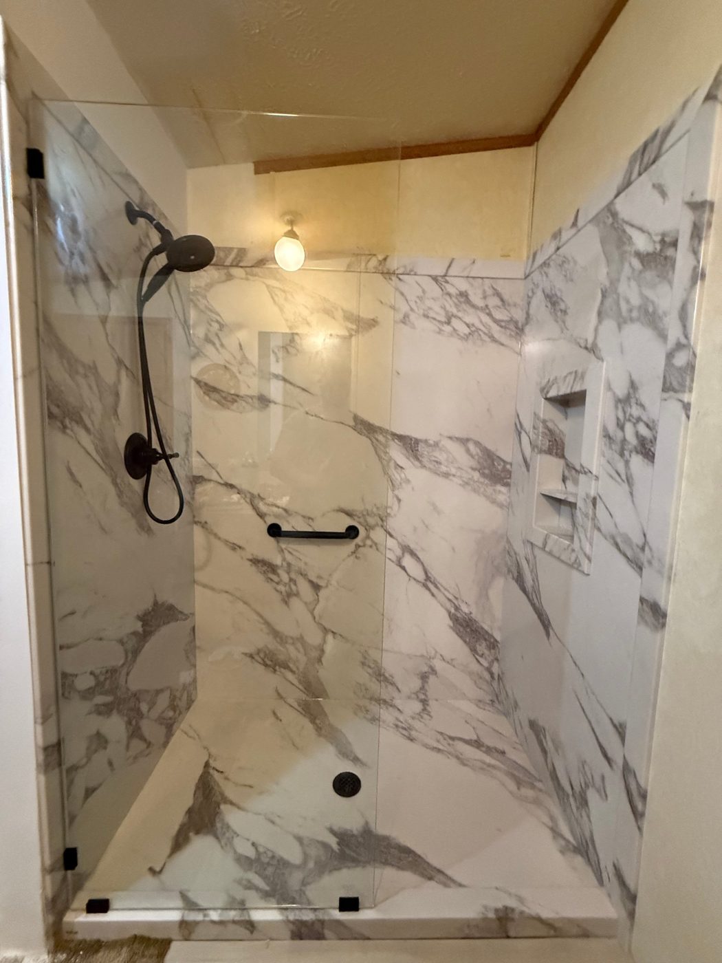 Walk-in shower with large white marble-look wall panels, a built-in niche, frameless glass and matte black fixtures